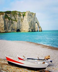 two boats sitting on the beach next to an ocean with cliffs and blue water in the background