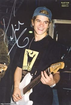 a young man holding a white guitar in his right hand and smiling at the camera