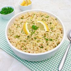 a white bowl filled with rice and lemon wedges next to two bowls of parsley