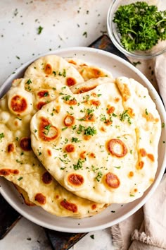 three flatbread pizzas on a white plate with parsley next to it and another dish in the background