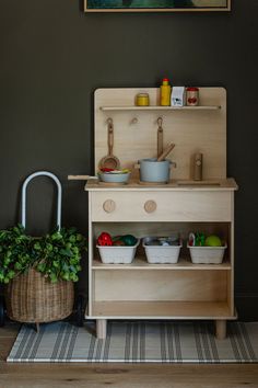 an old fashioned wooden toy kitchen with pots and pans on the stove top, in front of a green wall