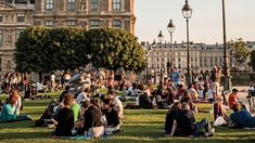 many people are sitting on the grass in front of buildings