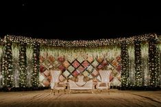 a stage set up for a wedding with two chairs and flowers on the back wall