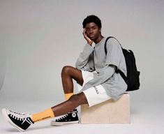 a young man sitting on top of a white block wearing black and yellow socks, a gray sweatshirt and backpack