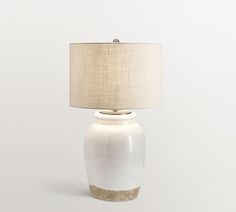 a white table lamp with a beige shade on the base and a light brown drum