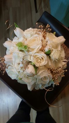 a bouquet of white flowers sitting on top of a black chair next to a person's legs