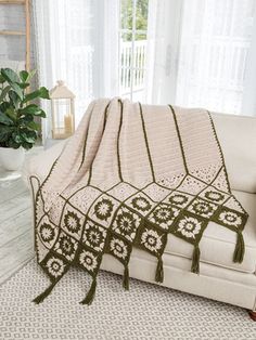 a white couch with a green crocheted blanket on it's back and a potted plant in the background