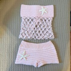 two pieces of pink knitted clothing with starfish on them, sitting on top of a bed