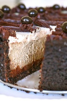 a chocolate cake with white frosting and black olives on top is cut in half