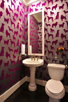 a white toilet sitting next to a sink in a bathroom under a mirror with dogs on it