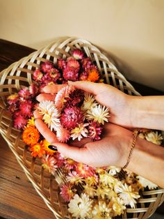 a woman's hand holding flowers in a basket on top of a wooden table