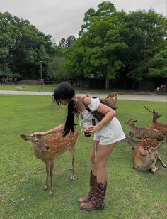 a woman standing next to a deer in a field