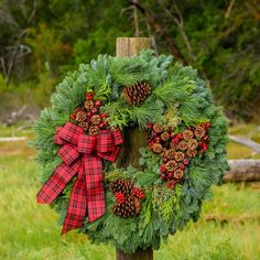 a christmas wreath with pine cones and evergreens on a wooden post in the grass