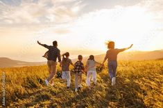 a group of people walking across a grass covered field with their arms in the air