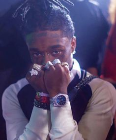 a young man with his hands on his face, wearing two different rings and looking at the camera