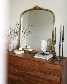 a large mirror sitting on top of a wooden dresser next to a vase with flowers