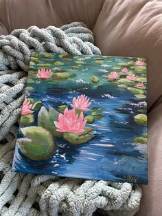 a painting of pink water lilies on a blue pond surrounded by white pillows and blankets