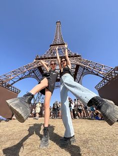 two people standing in front of the eiffel tower with their arms up and legs crossed