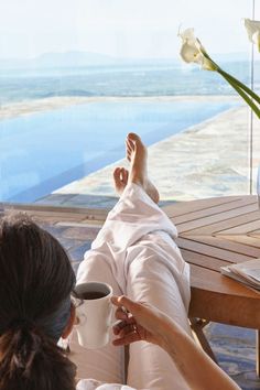 two women are sitting on a deck with their feet in the air and one is holding a coffee cup