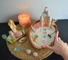 a person's hand is pointing at a miniature castle on top of a wicker tray