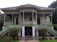 an old style house with green trim and balconies on the second floor, surrounded by greenery