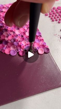 a person is using a marker to paint pink and purple dots on a piece of paper