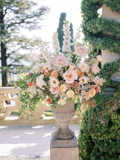 a vase filled with lots of flowers sitting on top of a stone bench next to a wall