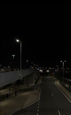 an empty road at night with street lights on the side and dark sky in the background