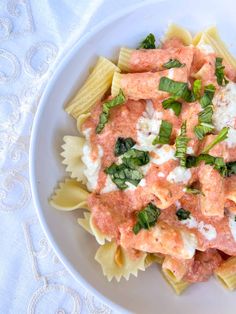 a white plate topped with pasta covered in sauce and spinach garnished with cheese