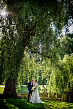 a bride and groom standing under a large tree