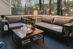 a couch and coffee table on a deck with lights strung above the porch railings