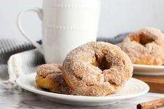 two sugared donuts are on a plate next to a cup and cinnamon sticks