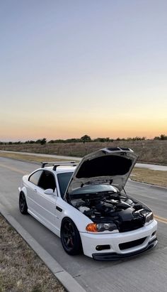 a white car is parked on the side of the road with its hood up open