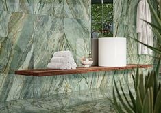 a bathroom with green marble walls and flooring next to a shelf filled with white towels