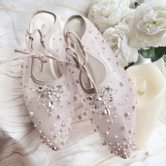 a pair of pink shoes sitting on top of a bed next to white flowers and a vase