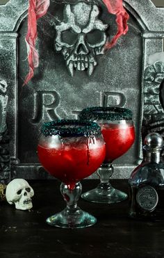 two glasses filled with red liquid sitting on top of a table next to a tombstone