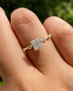 a woman's hand with a diamond ring on top of her finger, in front of some trees