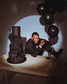 a man sitting at a table with two cakes and balloons