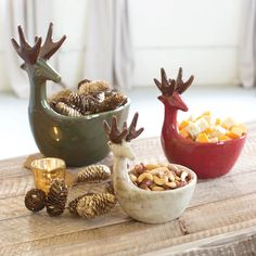 two bowls filled with nuts and reindeer antlers on top of a wooden table next to pine cones