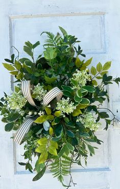 a bouquet of green leaves and white flowers on a doorknob with a bow