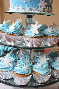 cupcakes with blue frosting and white snowflakes on them are stacked on a cake stand