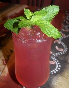 a close up of a drink in a glass on a table with a green leafy garnish