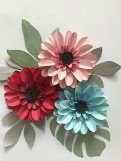 three paper flowers on top of each other with green leaves and one pink flower in the middle