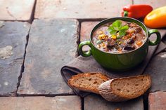 a bowl of soup and some bread on a stone floor with tomatoes in the background