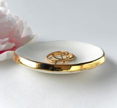 two gold wedding rings sitting on top of a white plate next to a pink flower