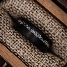 a black wedding band sitting on top of a piece of wood in a wooden box