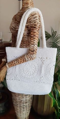 a woven white bag sitting on top of a wicker basket next to a plant