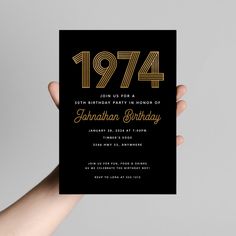 a hand holding up a black and gold birthday card with the year 1974 printed on it