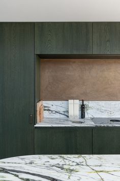 a marble counter top in a kitchen with green cabinetry and wooden shelves above it