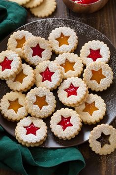 small cookies with jelly filling on a black plate next to a bowl of jam and a green napkin